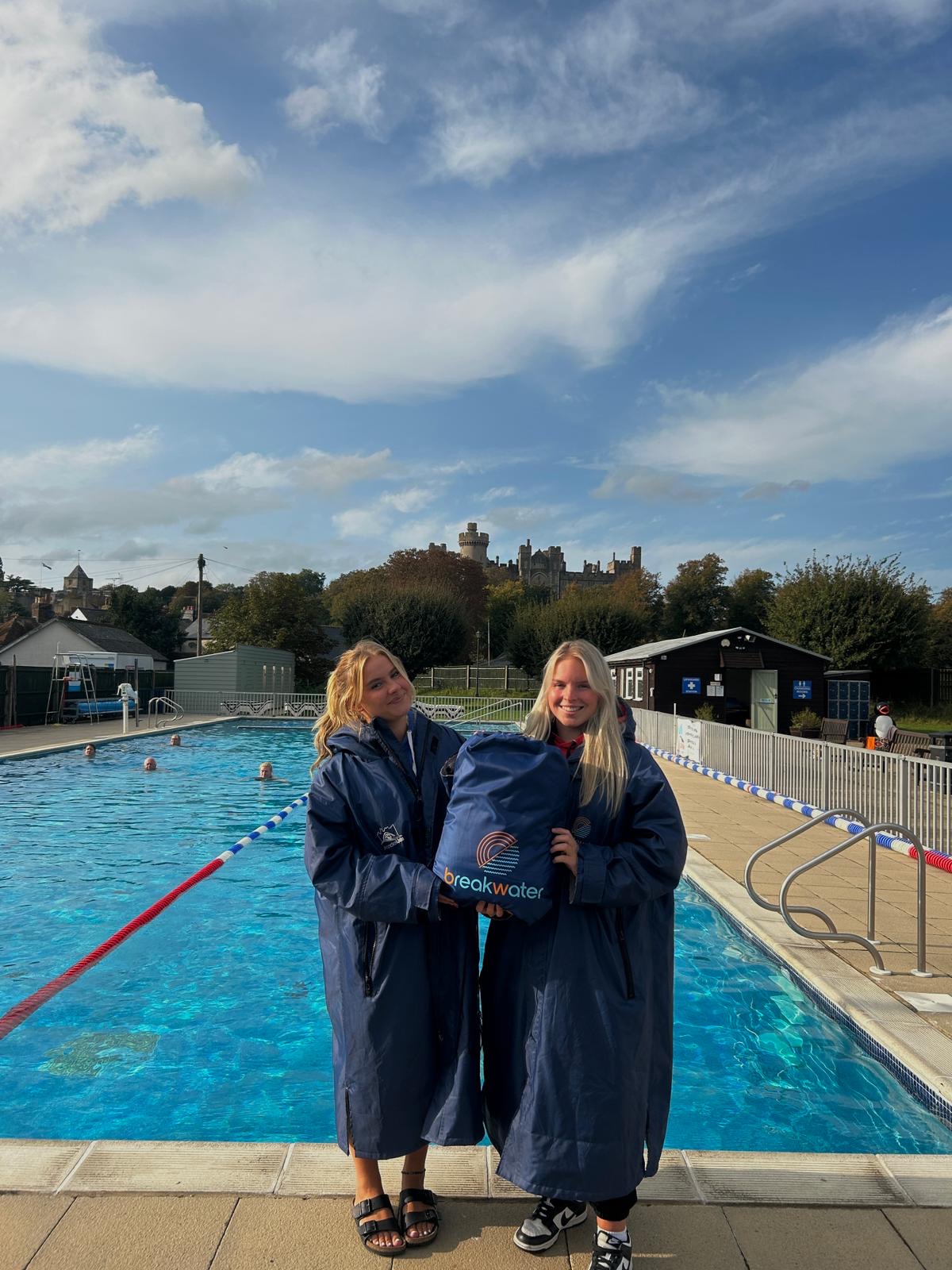 Two women standing by the side of Arundel Lido's outdoor swimming pool. Between them is a blue bag with 'breakwater' written on it.