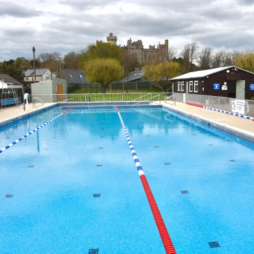 A portrait image of Arundel Lido's outdoor pool with Arundel Castle in the background.